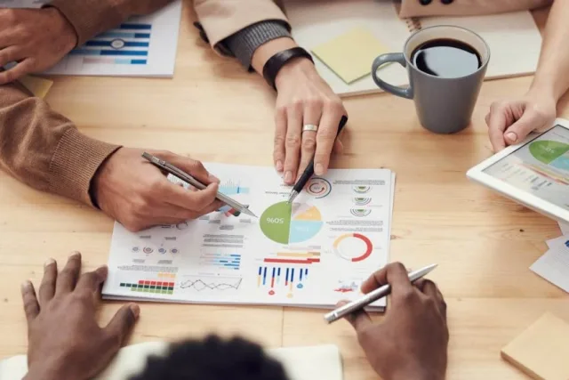 Four people around a table annotating a printed page of charts