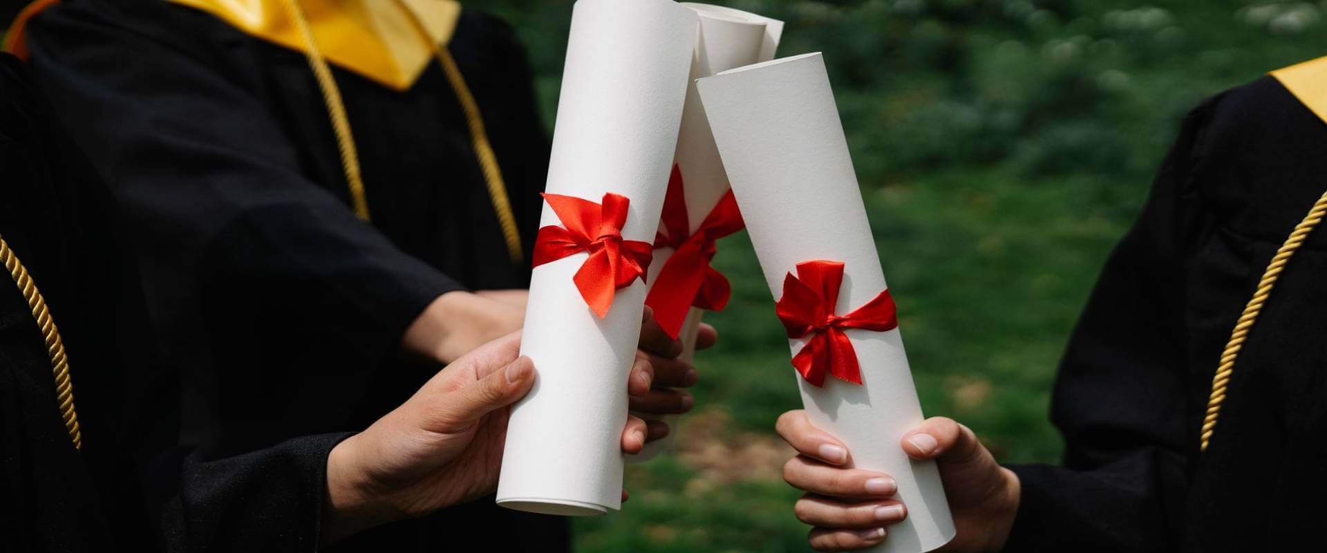 Graduates in black gowns holding rolled diplomas tied with red ribbons