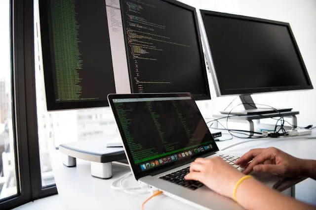 A developer writing code across a laptop and two monitors
